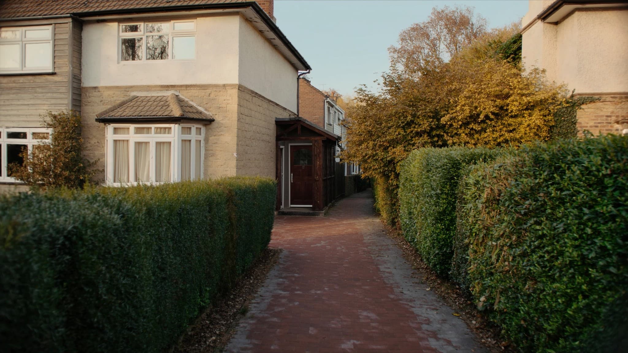 A narrow brick path running between clipped hedges to the side door of a British semi