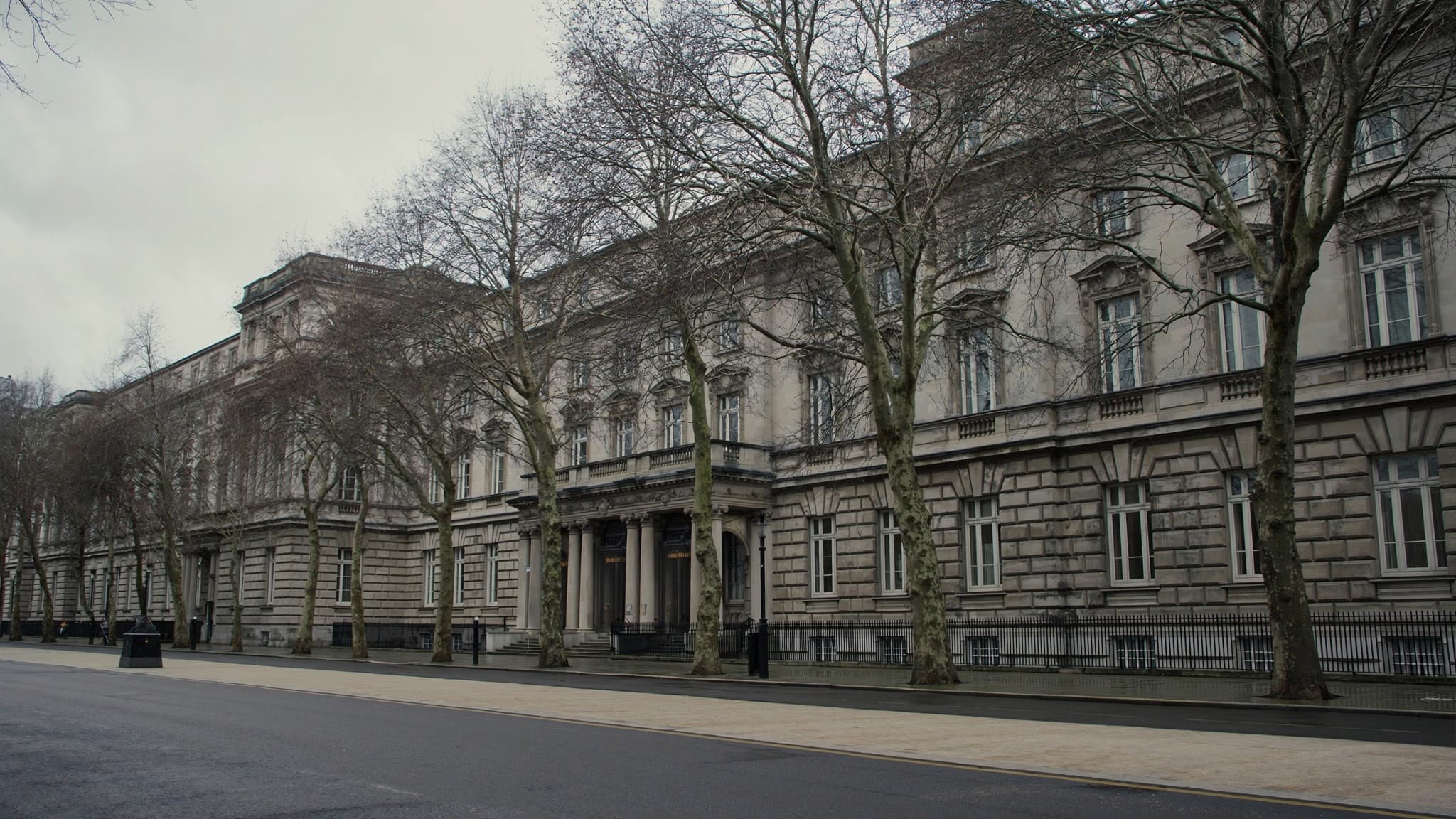 The long stone facade of a government building behind bare winter trees