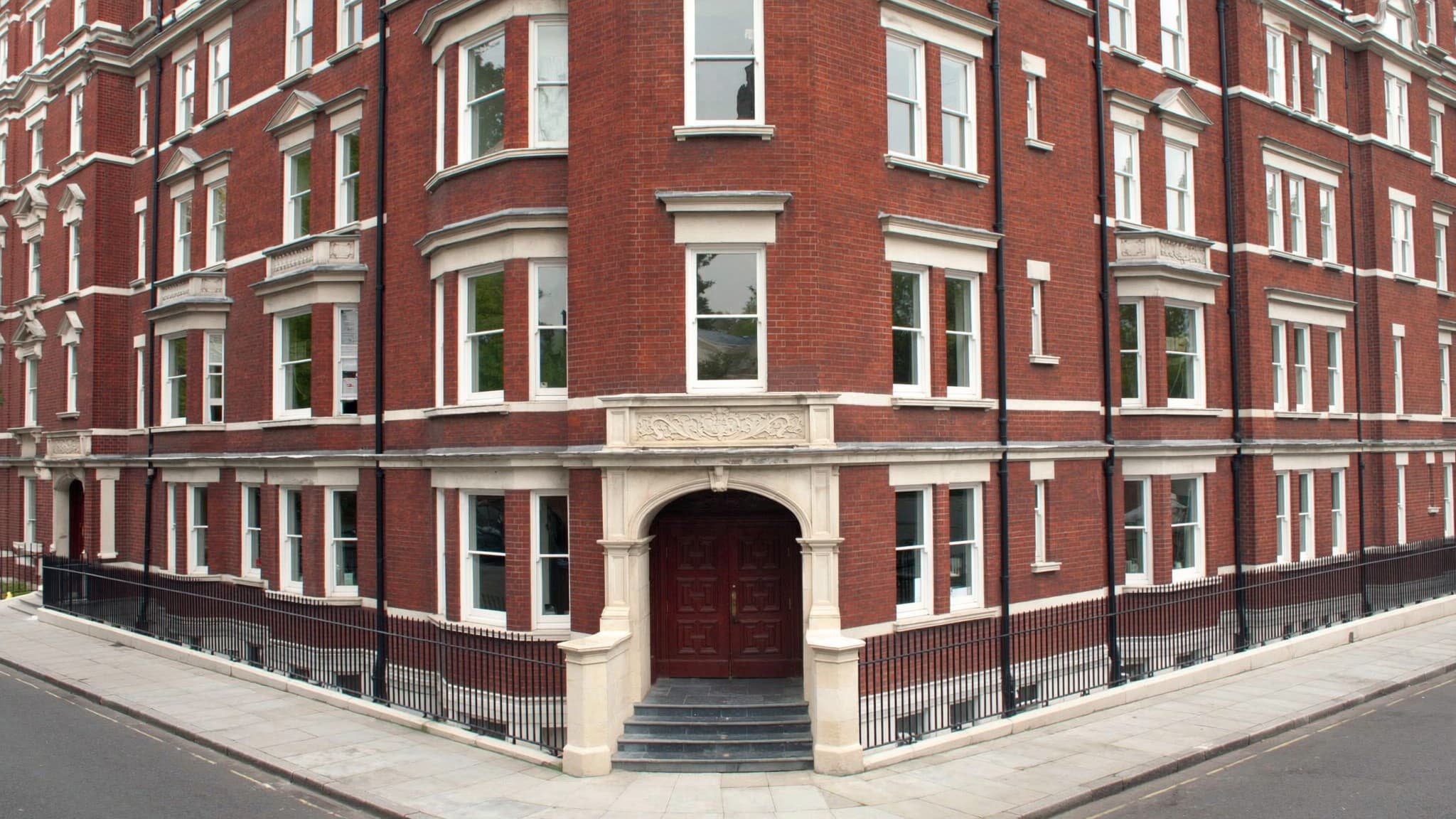 The corner of a red brick Victorian mansion block with stone detailing around the entrance