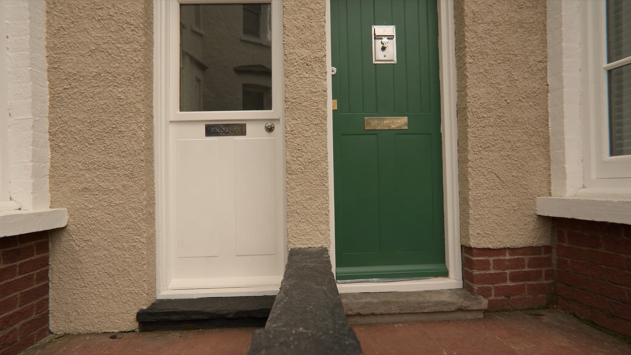 A green painted front door in a brick porch with an entry phone beside it
