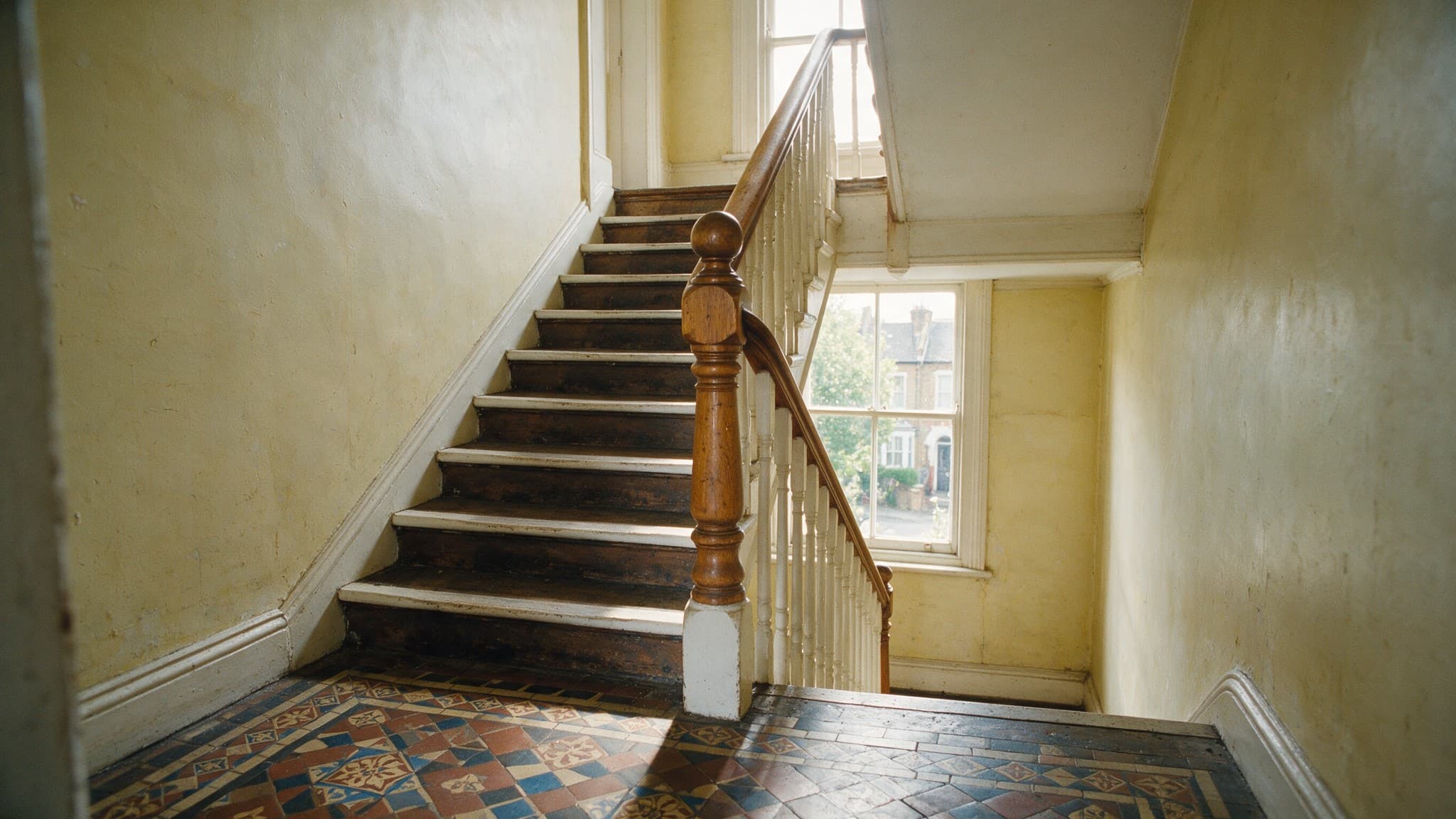 A communal staircase in an older converted building, tiled hallway floor at the foot