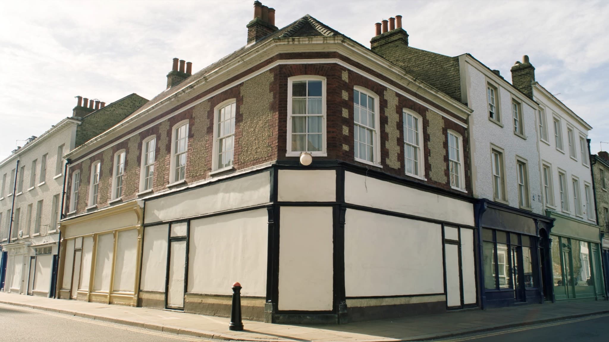 A corner parade of shops on a British high street with blank shopfronts below