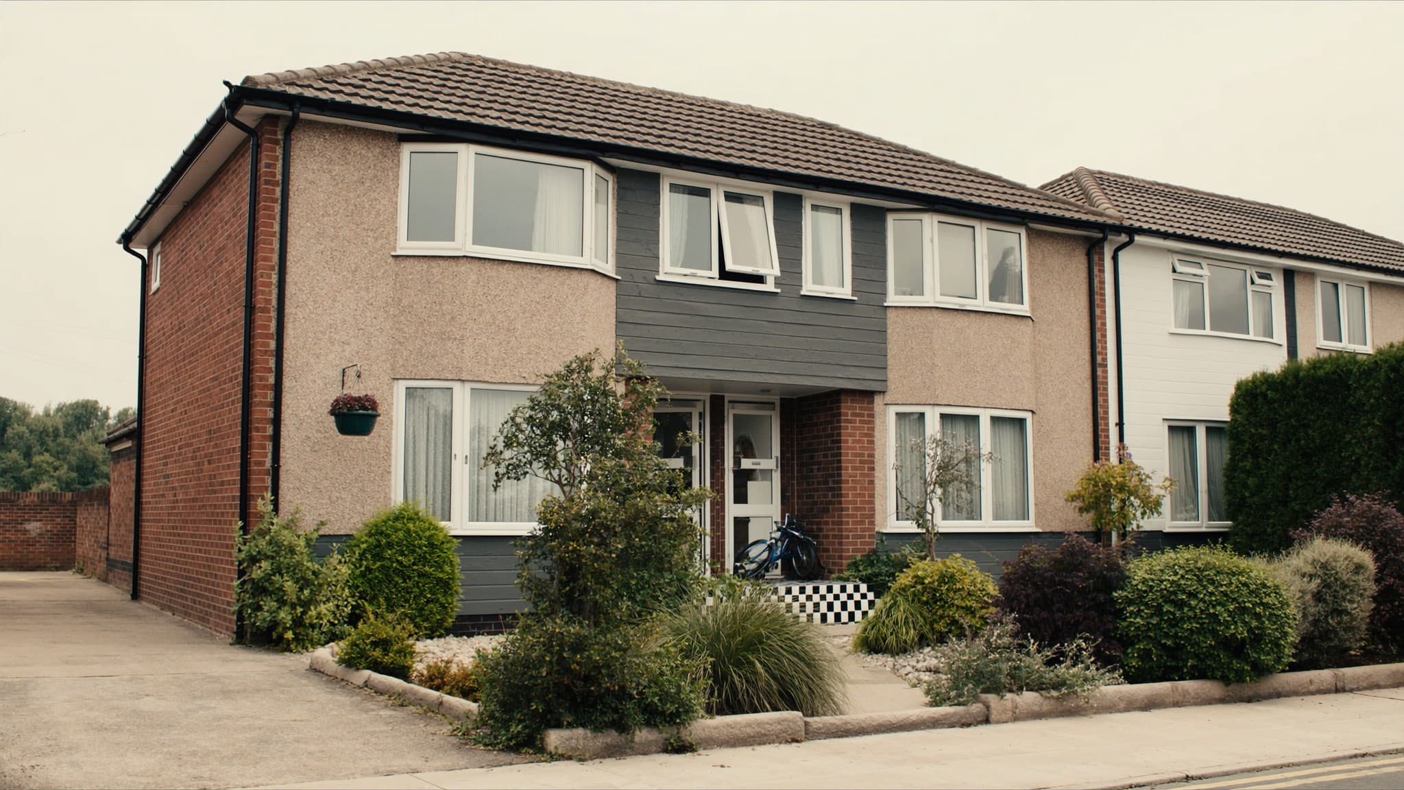 A brick semi-detached house with a planted front garden and a bay window
