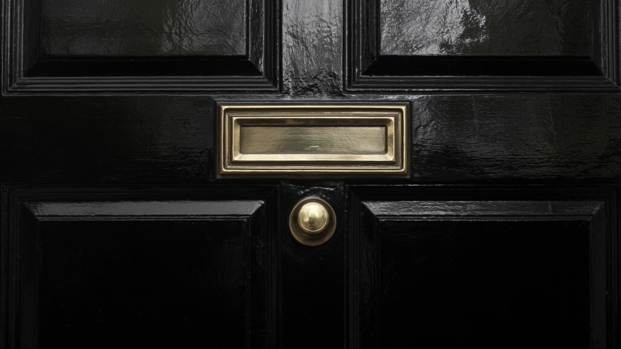 A black panelled front door with a polished brass letterplate and knob