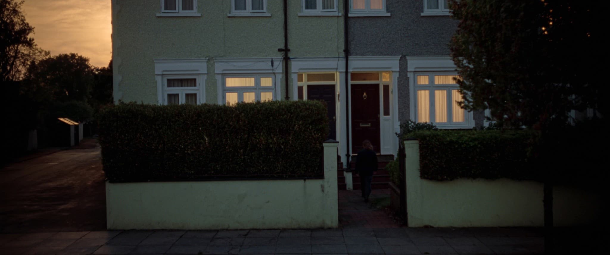 A buyer reaching a front door at dusk on a quiet suburban street.