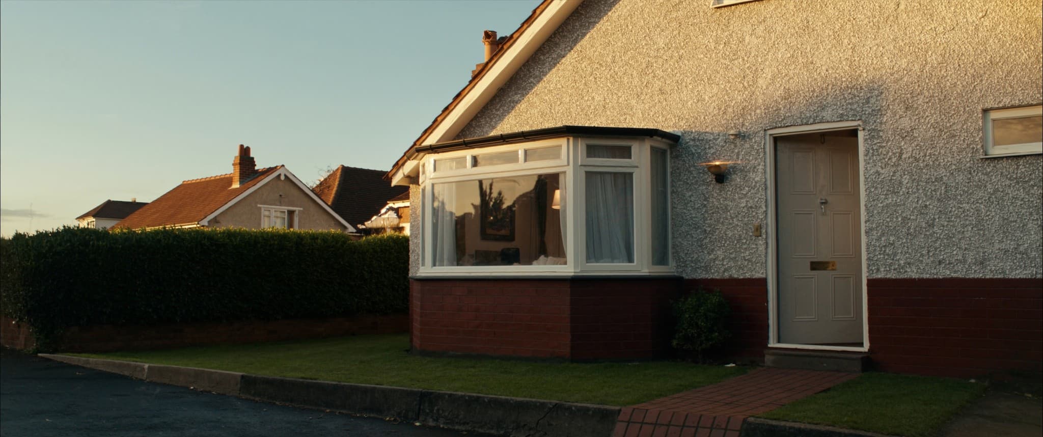 A 1930s bay fronted semi in low evening light, curtains open and a light on inside