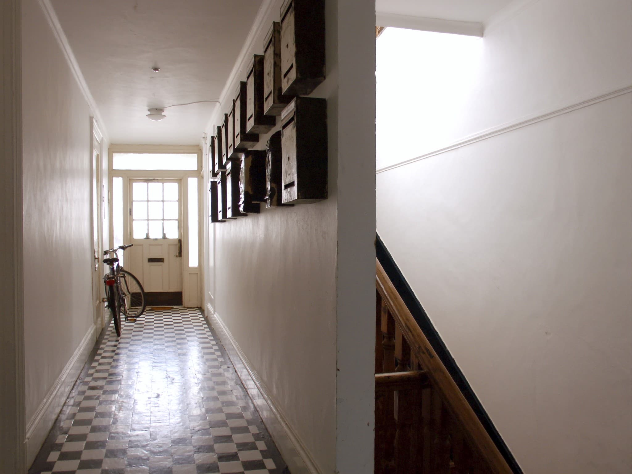 The bright communal entrance hall of a British Victorian house converted into flats, letterboxes on the wall and a bicycle by the stairs