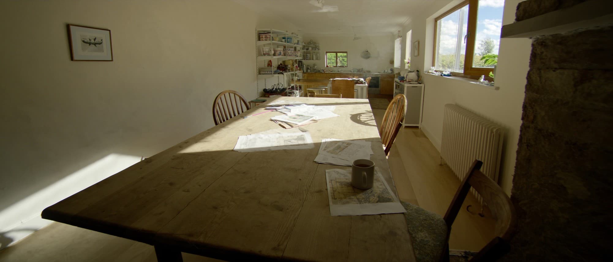 The paperwork of a house purchase spread across a sunlit kitchen table, a fanned stack of pages, an opened property plan and a mug of tea