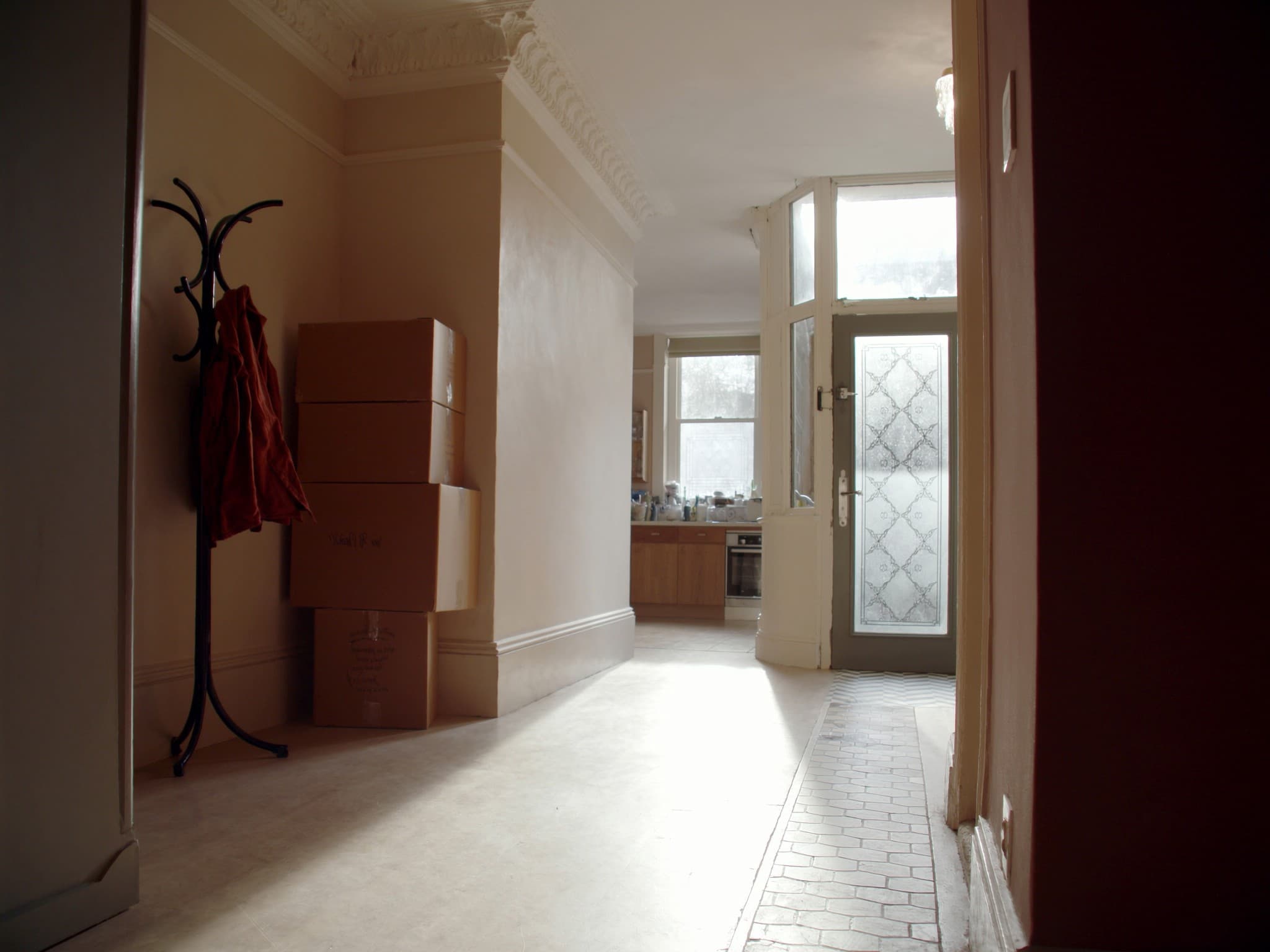 A British hallway on moving morning, boxes stacked by the front door with coats still hanging above them