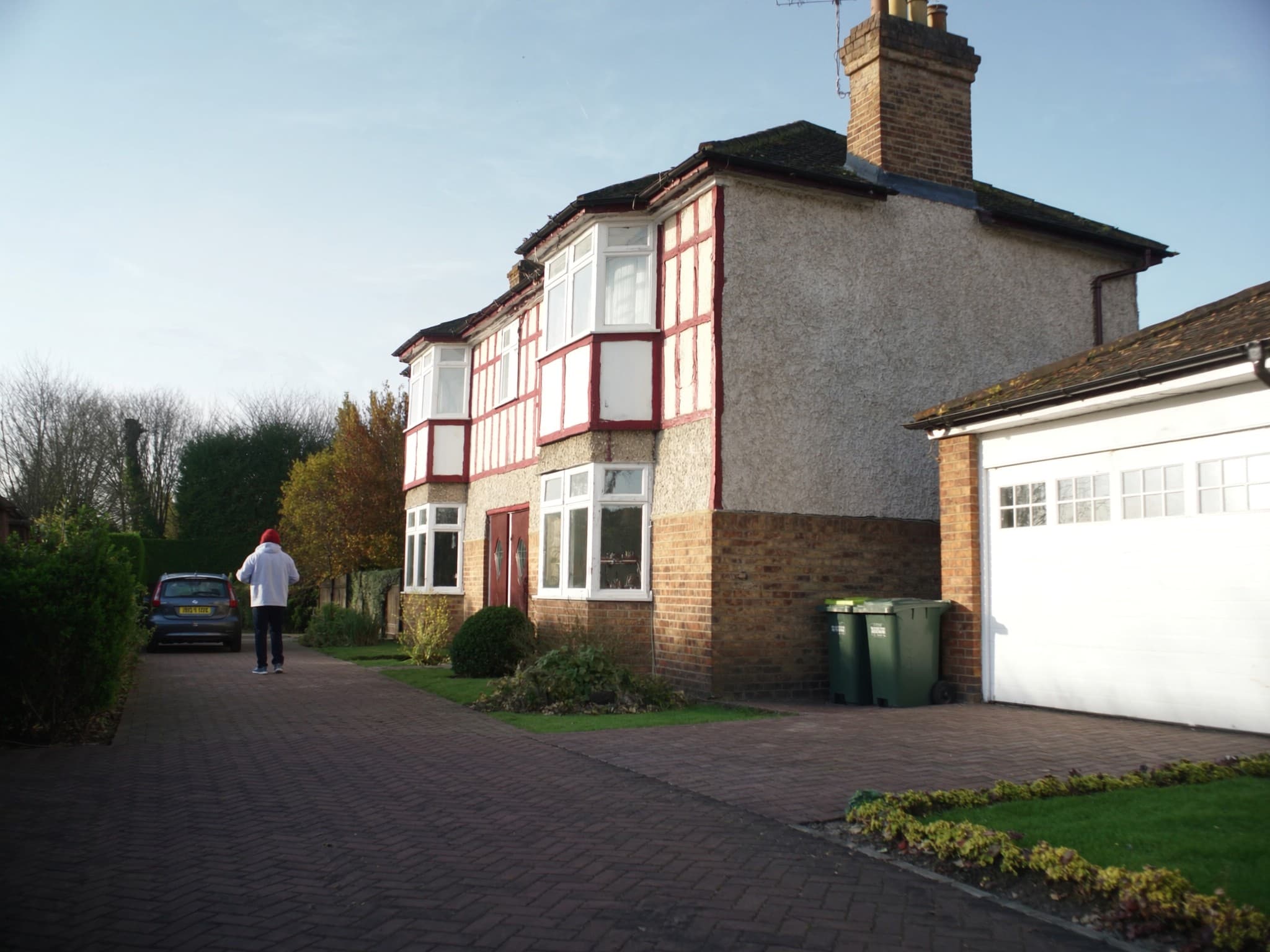 The front of an ordinary British 1930s semi on a bright day, a car on the drive and a trimmed hedge