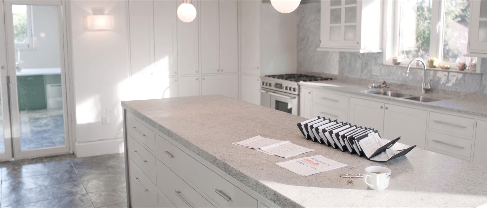 A seller's paperwork gathered along a bright kitchen island, a full document wallet, a folded plan and a bunch of window keys