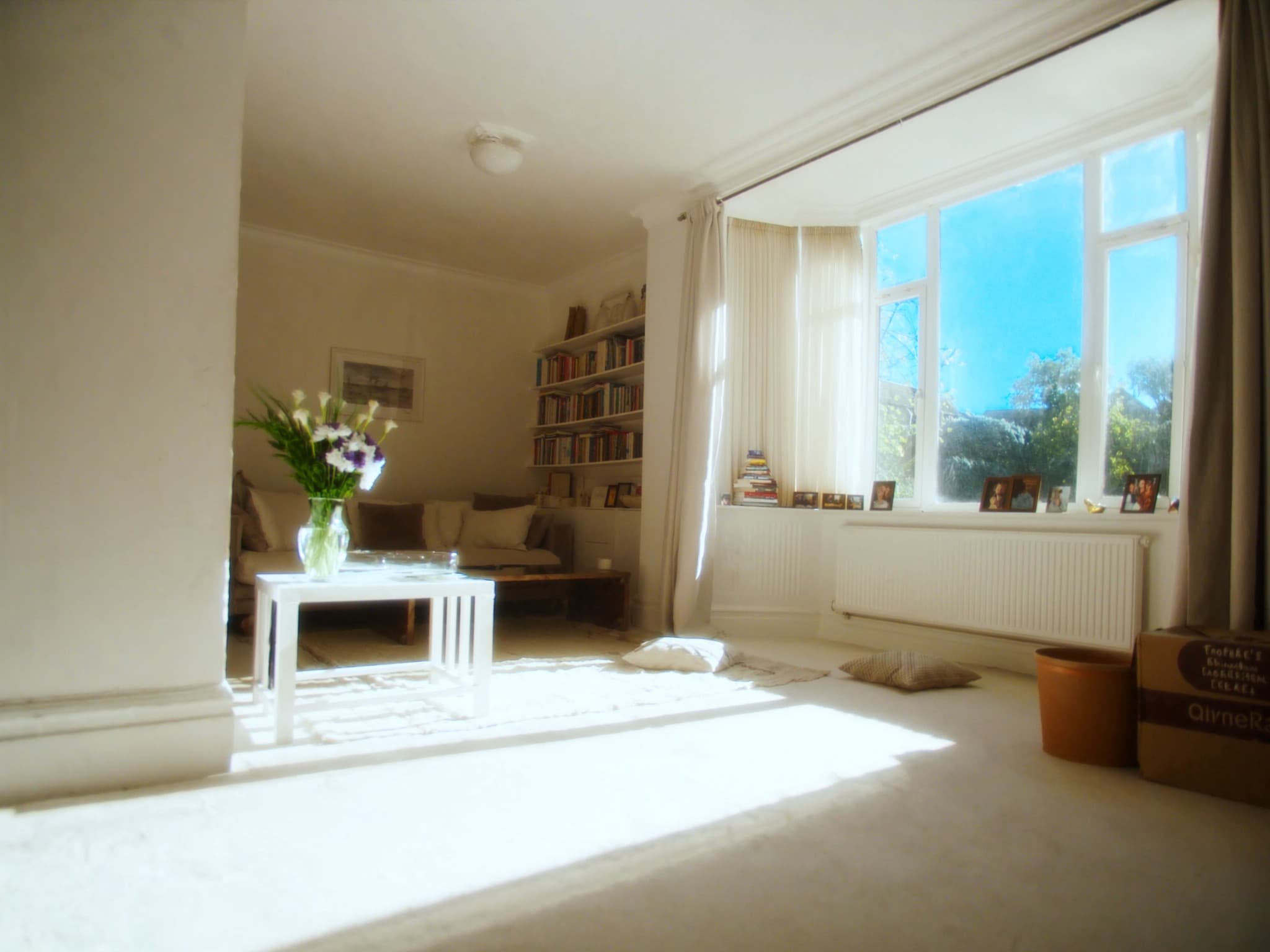 A tidy sitting room in an ordinary British home ready for a viewing, sun through a sash window onto a rug and straightened cushions