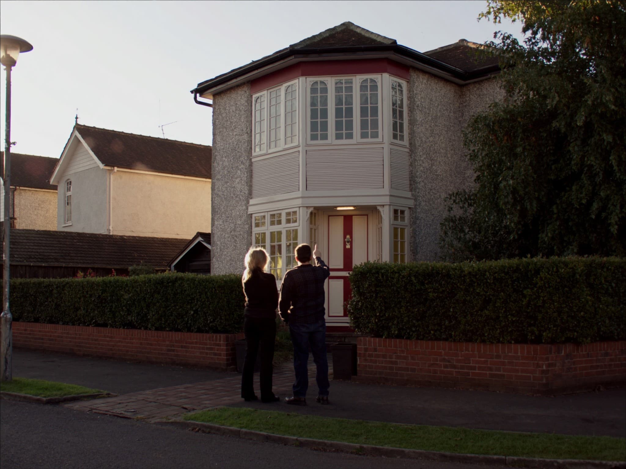A couple standing at the front gate of a British semi-detached house, looking up at it together