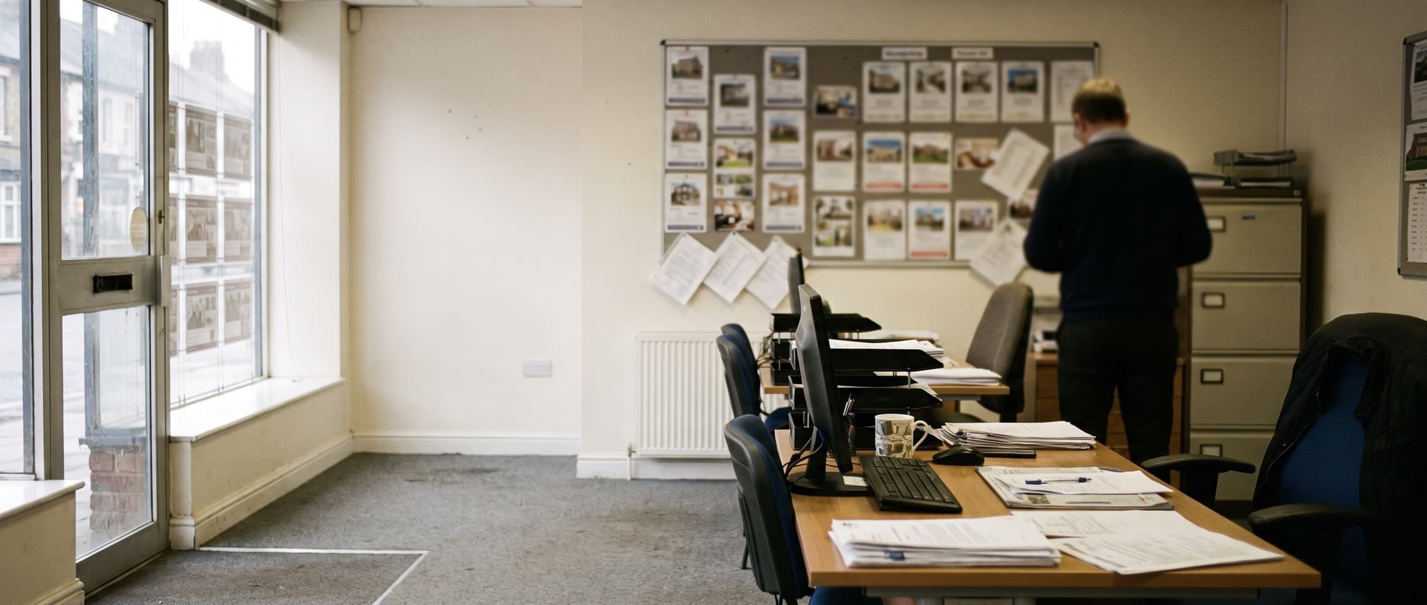The inside of a small British high street estate agency, desks and a wall of property cards