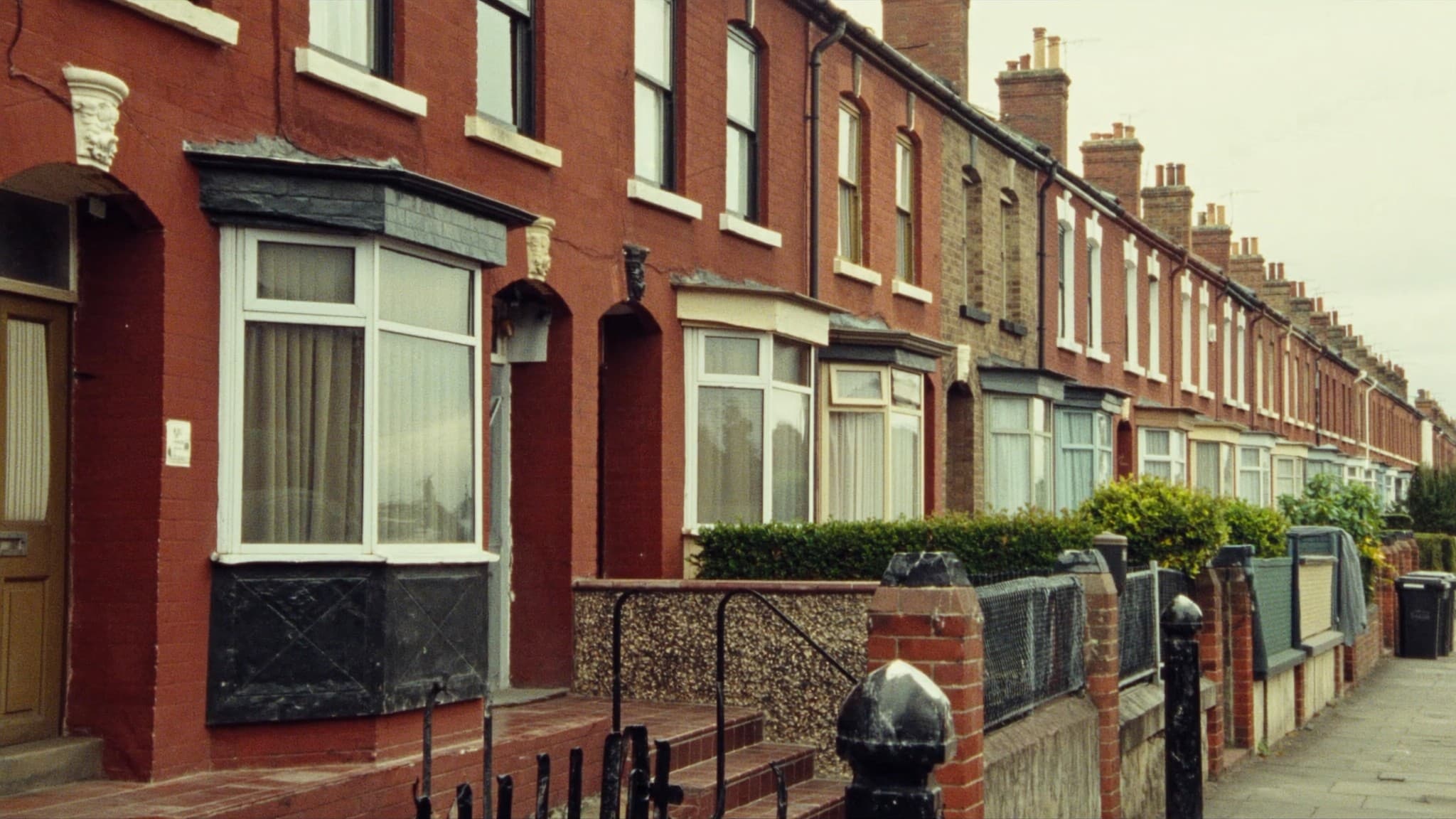 An unbroken row of red-brick British terraced houses running away down a street